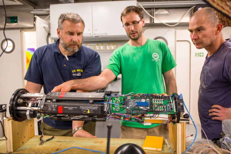 Richard Camilli, of Woods Hole Oceanographic Institution (blue shirt) speaks with Christopher Roman, University of Rhode Island (green hirt) about the photo-float operations and planning in the Wet Lab on Falkor. 