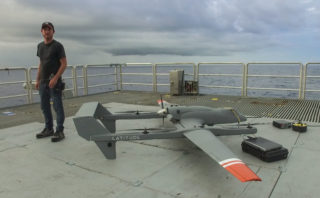 Scott Brown, Physicist and Engineer, stands next to one of the HQ-60B drones to scan the sea surface. The drone had just completed another successful mission and was being disarmed on Falkor's flight deck.