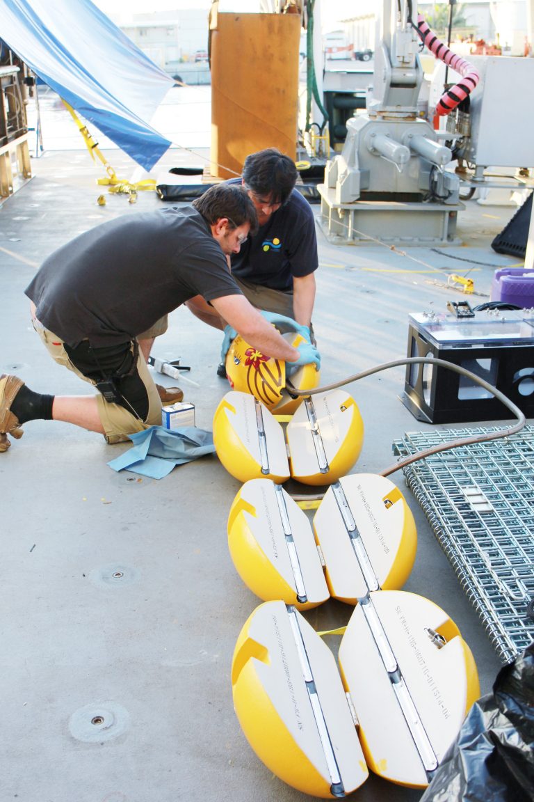Lead Marine Technician Leighton Rolley and Marine Technician James Cooper work on inserting the rubber into the umbilical floats.
