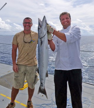 Chief Bosun Mick Utley hands off his barracuda catch to Chef Carlos Waihrich. 