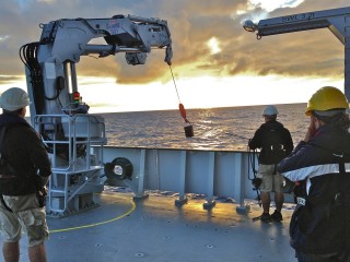 The crew using a crane and the metal bucket to collect a sample for Brandon's study.