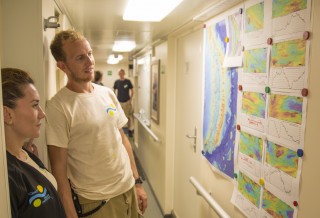 Crew members discuss where to place their bets while studying the maps of the 10 back-arc segments posted in the main hallway of R/V Falkor. 