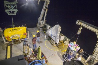 The autonomous underwater vehicle Sentry (yellow, at left) is prepared for deployment off the stern of the R/V Falkor, after a trace-metal CTD instrument package and water sampler is recovered (lower right). 