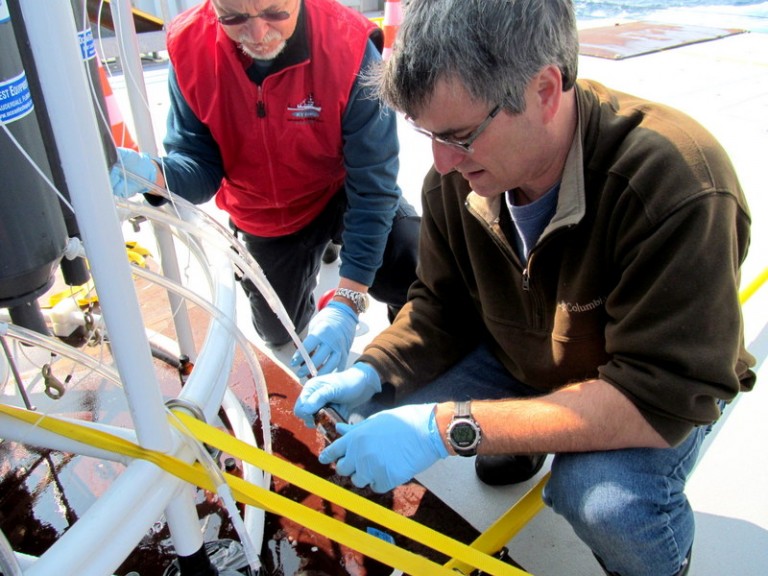 University of Rhode Island Professor David Smith (right) and URI lab manager Dennis Graham draw samples from the Conductivity, Temperature and Pressure Rosette on Saturday, July 21, 2012 aboard the R/V Falkor about 100 miles off the coast of Newfoundland.