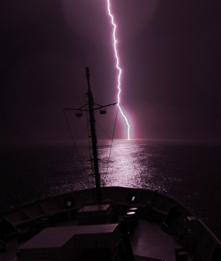 A bolt of lightning strikes off Falkor's bow.
